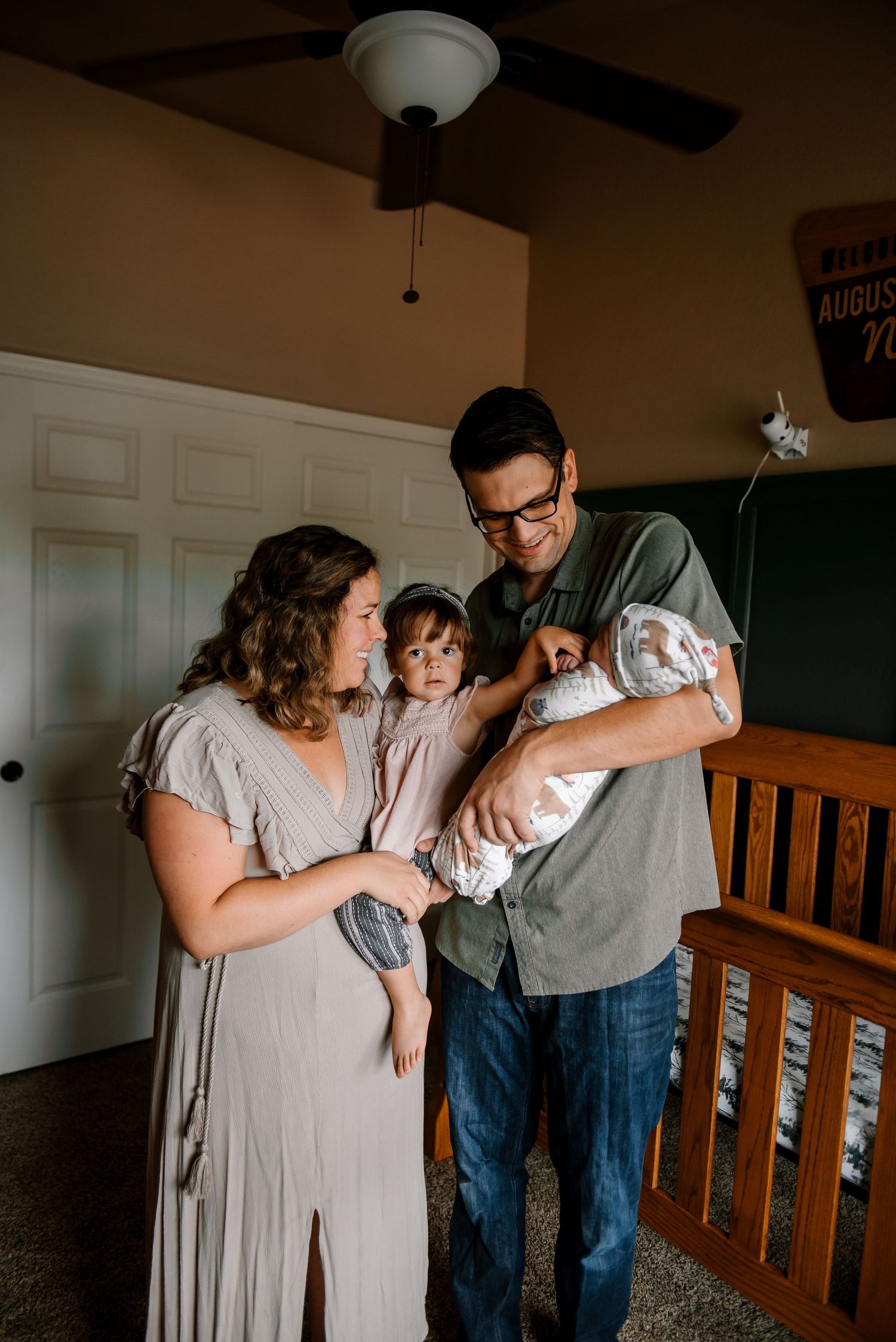 Family gathering around newborn baby in home nursery with wooden furniture.