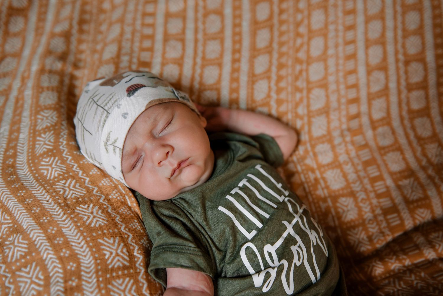 Baby sleeping peacefully on a patterned orange blanket.