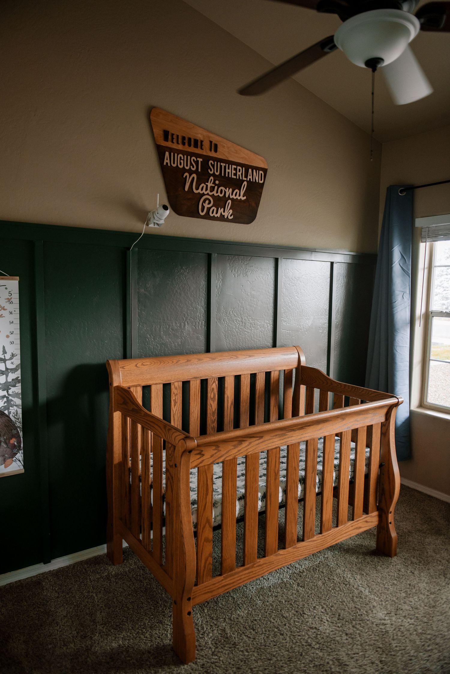 Wooden nursery furniture with a crib against dark green walls.