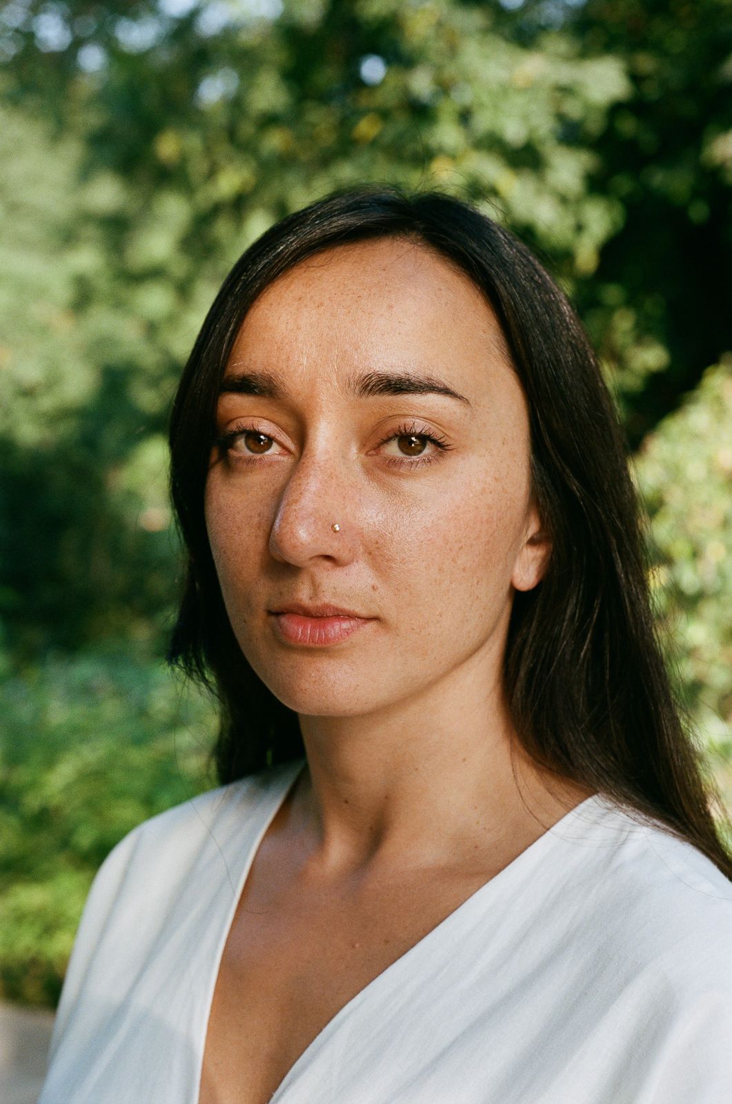 Portrait of a person with long dark hair wearing a white top against a green background.