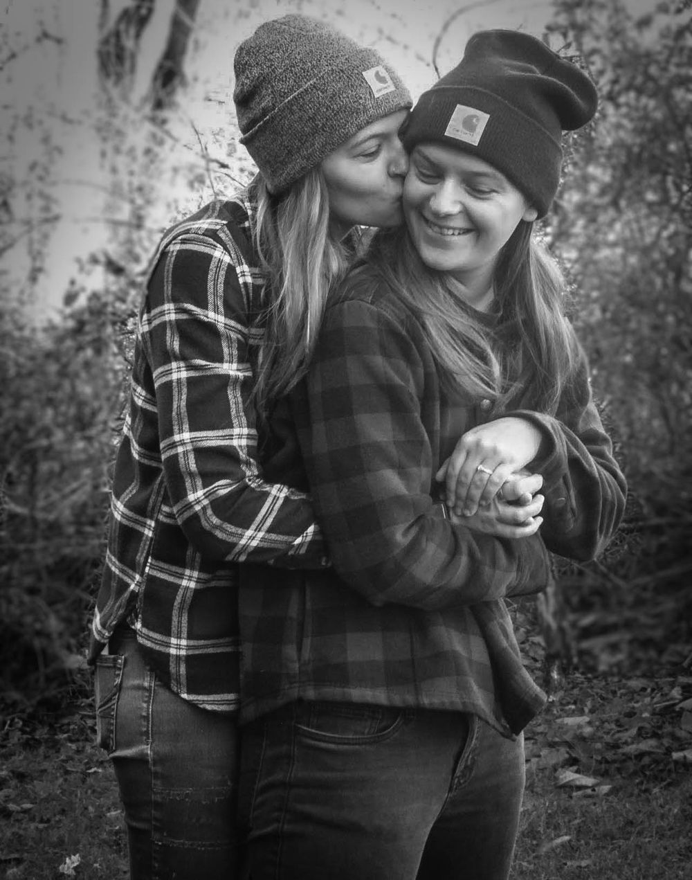 Black and white portrait of two people in plaid shirts sharing an intimate moment outdoors.