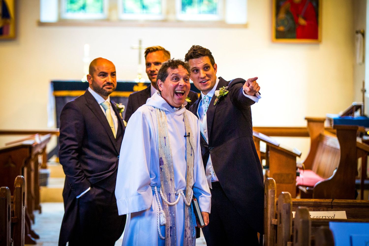 Wedding guests and clergy sharing laughter during a ceremony in a traditional church setting.