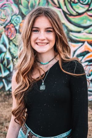 Portrait against colorful graffiti wall wearing black top and turquoise accessories.