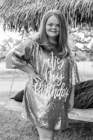 Person in sequined shirt sitting under thatched roof.