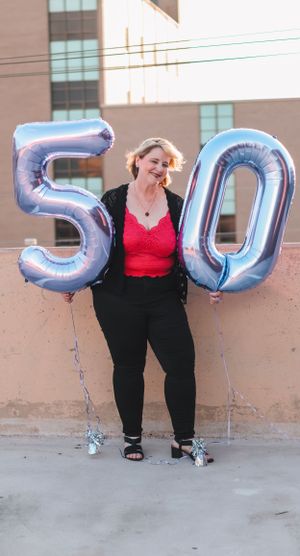 Person in red top poses with silver number balloons against beige wall.
