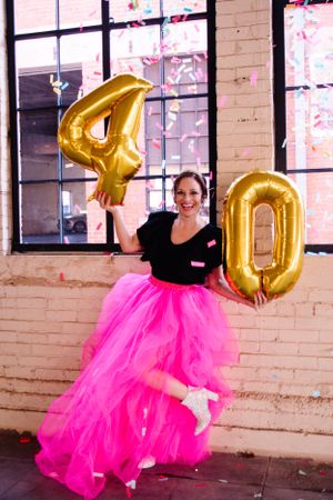 Celebration photo with pink tulle skirt and gold number 40 balloons in brick interior.