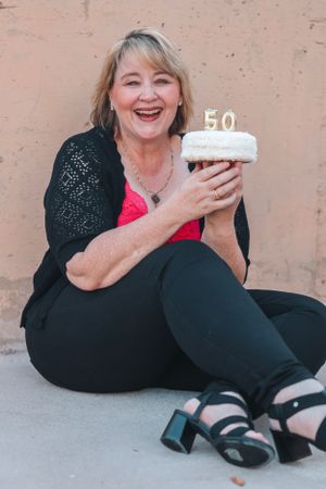 Person in black outfit celebrates milestone with cake on ground.