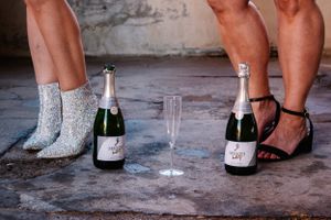 Close-up of feet and champagne bottles with glitter on the ground.