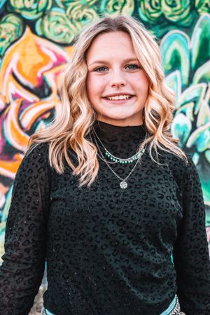 Portrait against graffiti wall wearing textured black turtleneck and silver necklace.