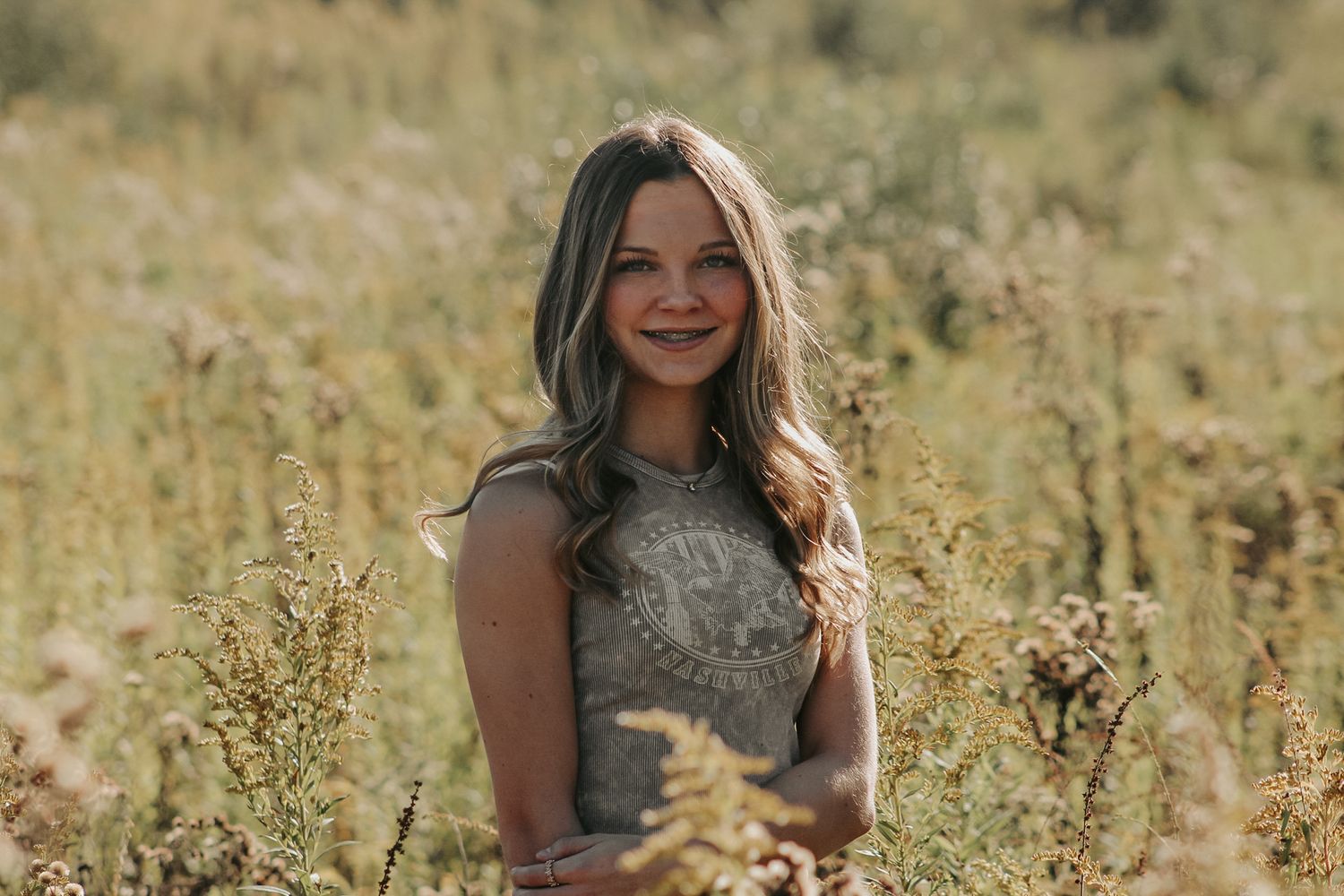 Sunset portrait in grey top amid natural meadow setting.