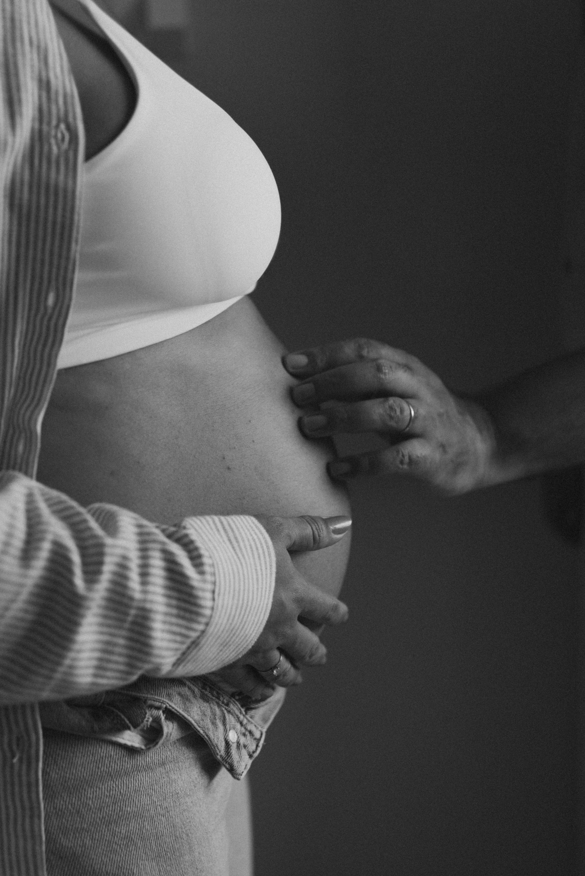 Close-up black and white photo of hands tenderly cradling a pregnant belly.