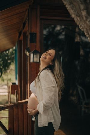 A joyful maternity portrait showing an expectant mother laughing on a rustic porch.