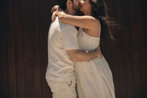 A romantic embrace between two people in white clothing against a dark background.