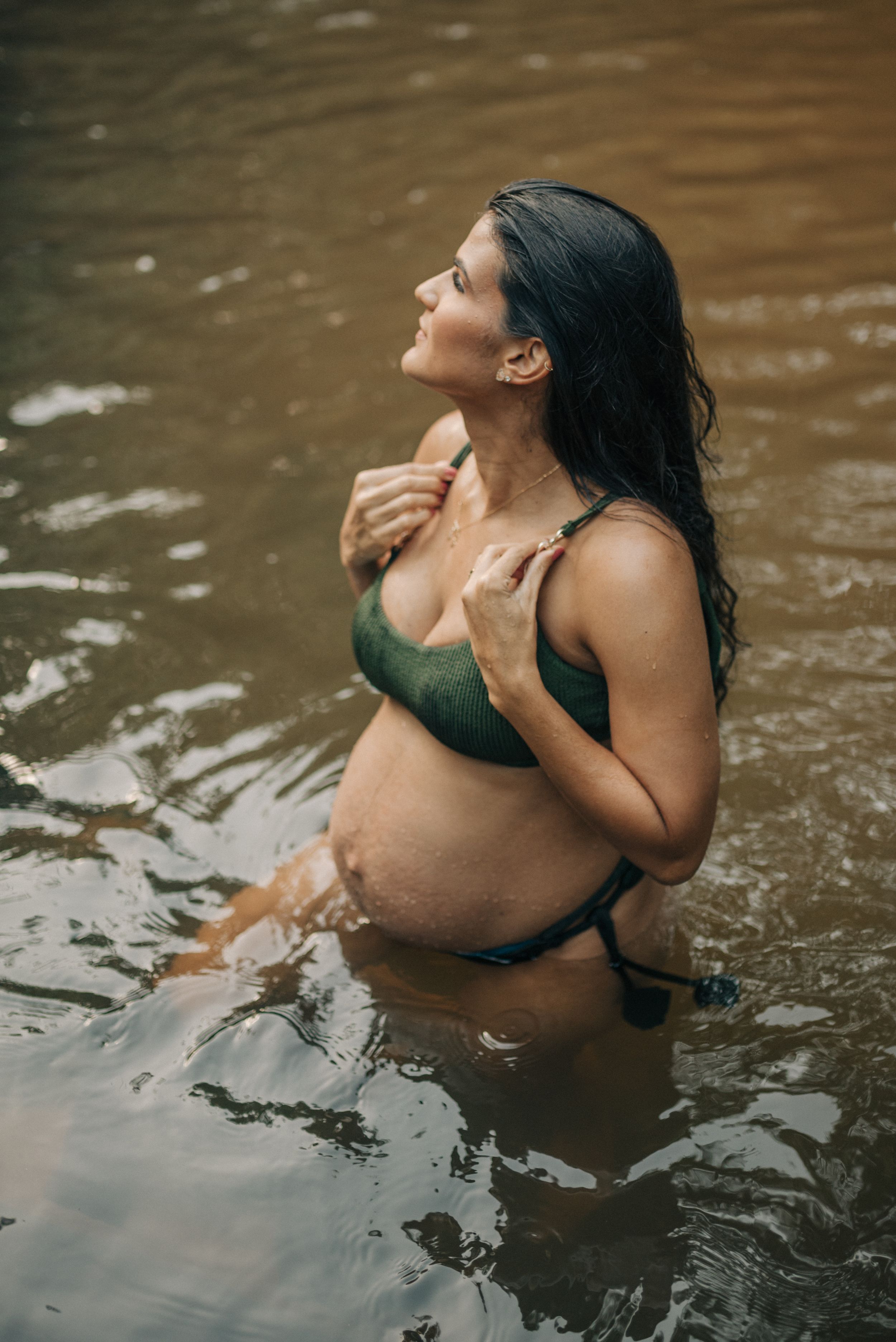 Pregnant woman in green swimsuit enjoys peaceful moment in brown-tinted water.