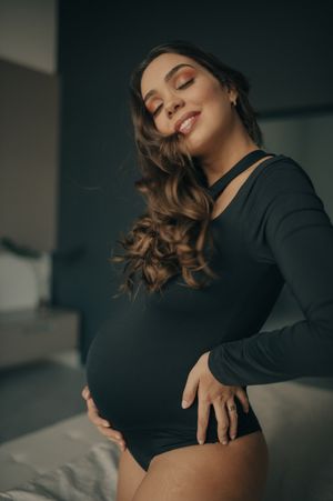 Maternity portrait in black bodysuit with warm indoor lighting.