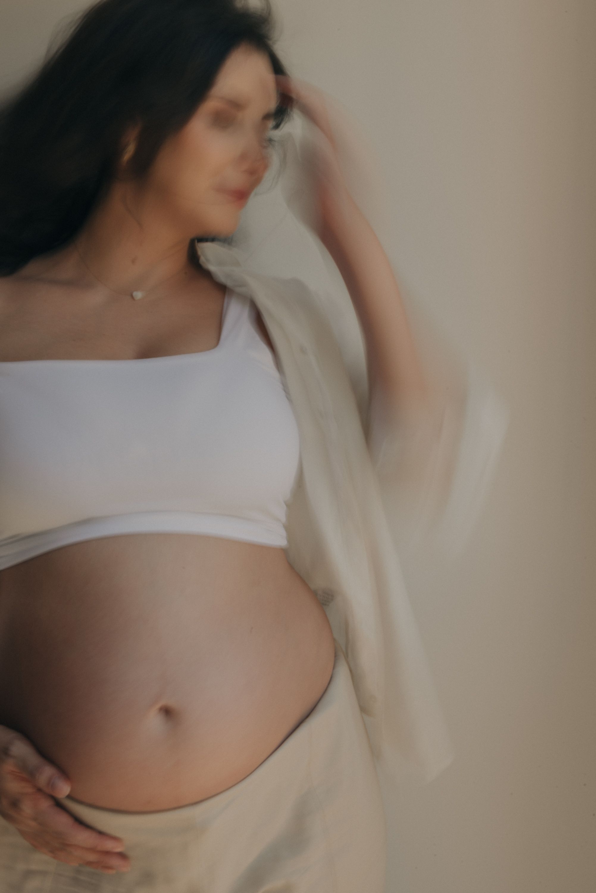 Soft focus portrait showing pregnant belly in white crop top and flowing fabric.