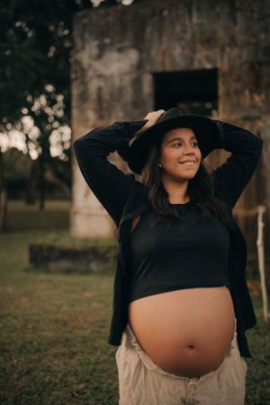 Candid outdoor maternity photo with person in black sweater against rustic wall.