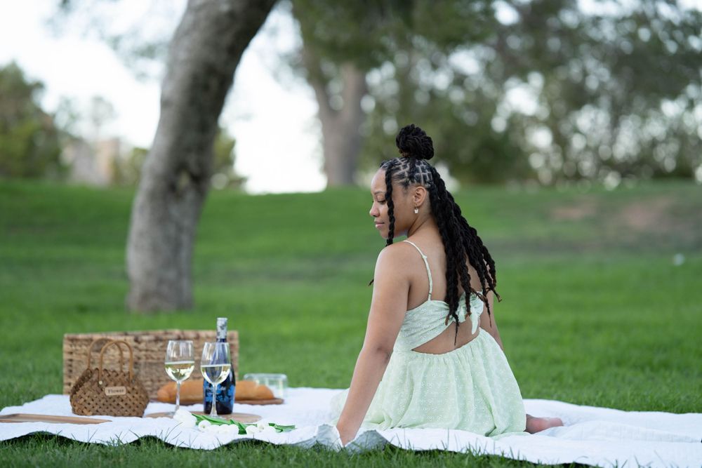 Someone in a mint dress sitting on a picnic blanket with a basket and drinks visible.