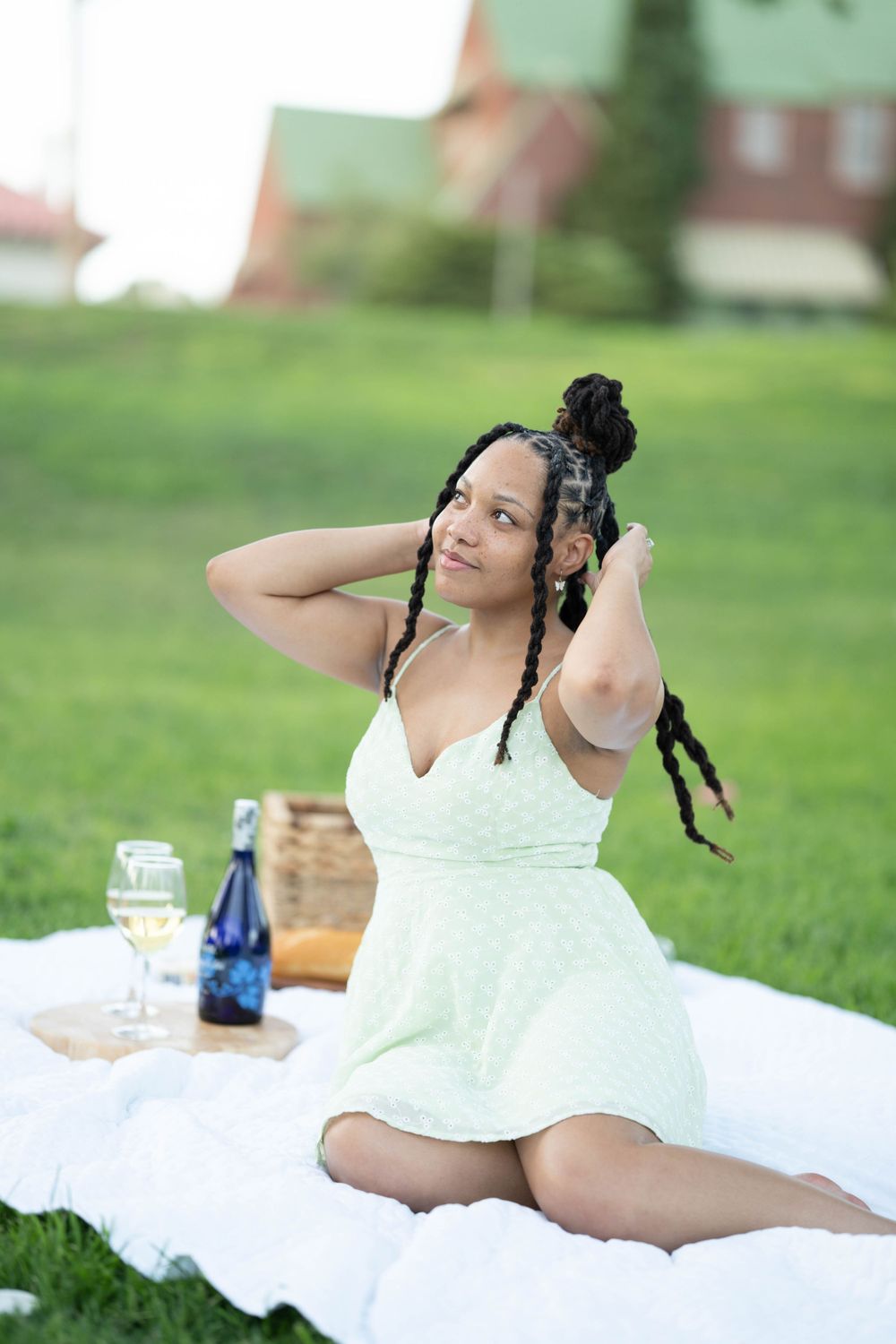 A picnic scene on a grassy lawn with a white blanket, wine bottle, and someone in a mint green dress lounging.