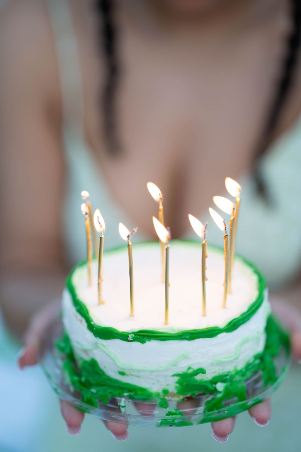 A close-up of a white and green birthday cake with lit gold candles on top.