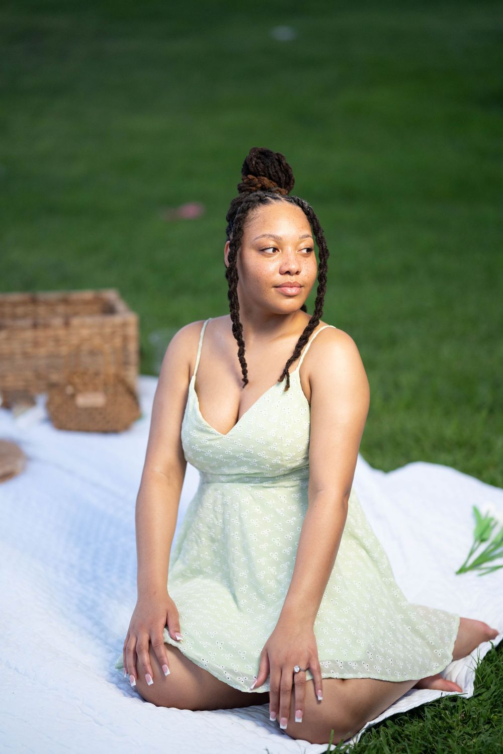 Person in light green dress posing on white blanket on grass.