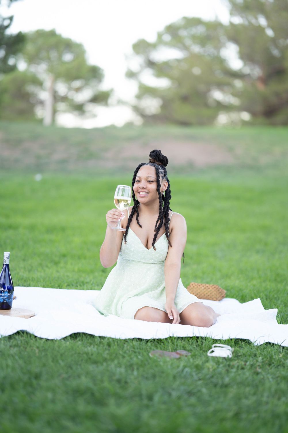 Person having picnic on white blanket with wine glass on grassy lawn.