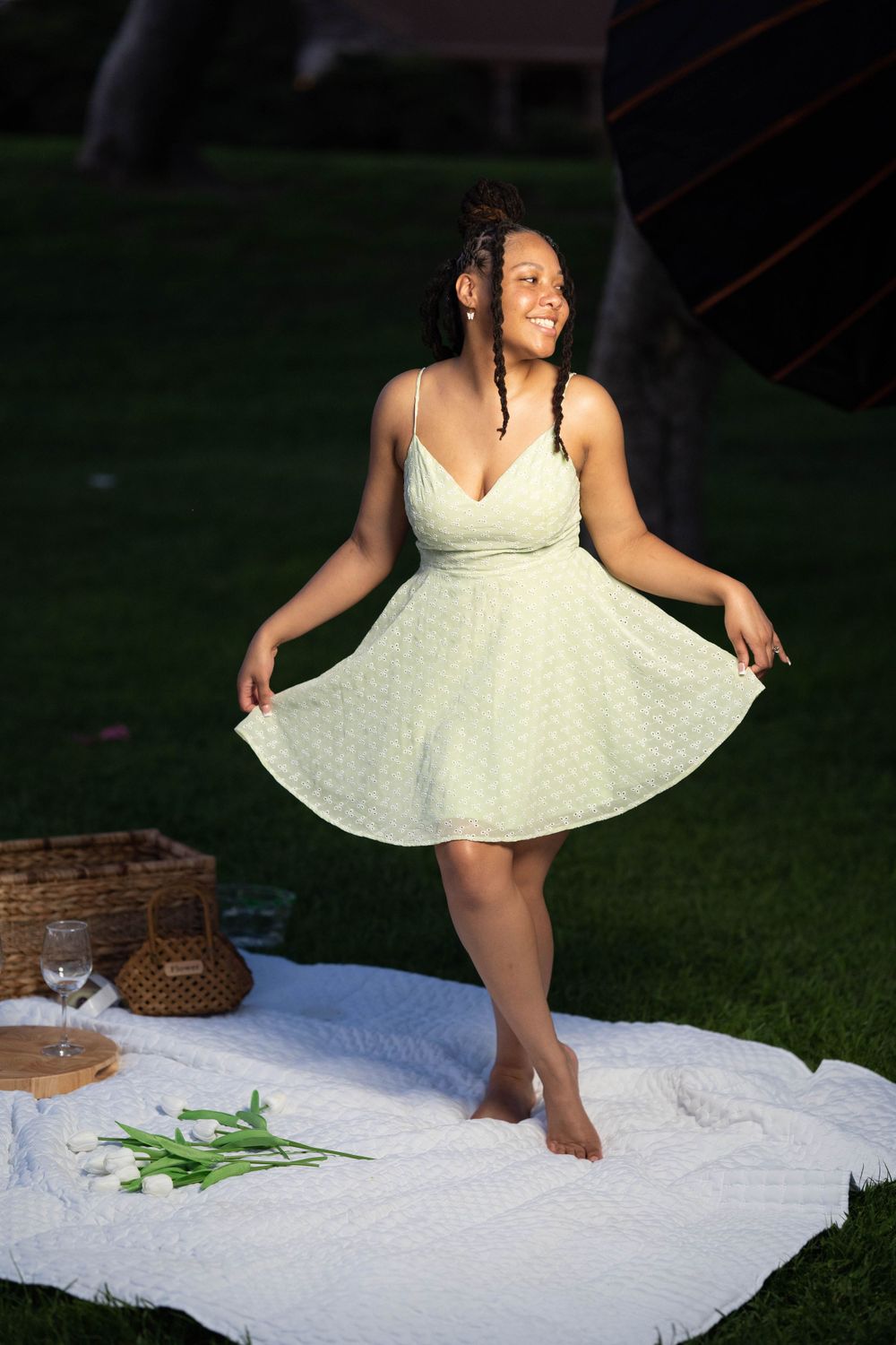 Person in flowy mint dress twirling during outdoor photoshoot on white blanket.