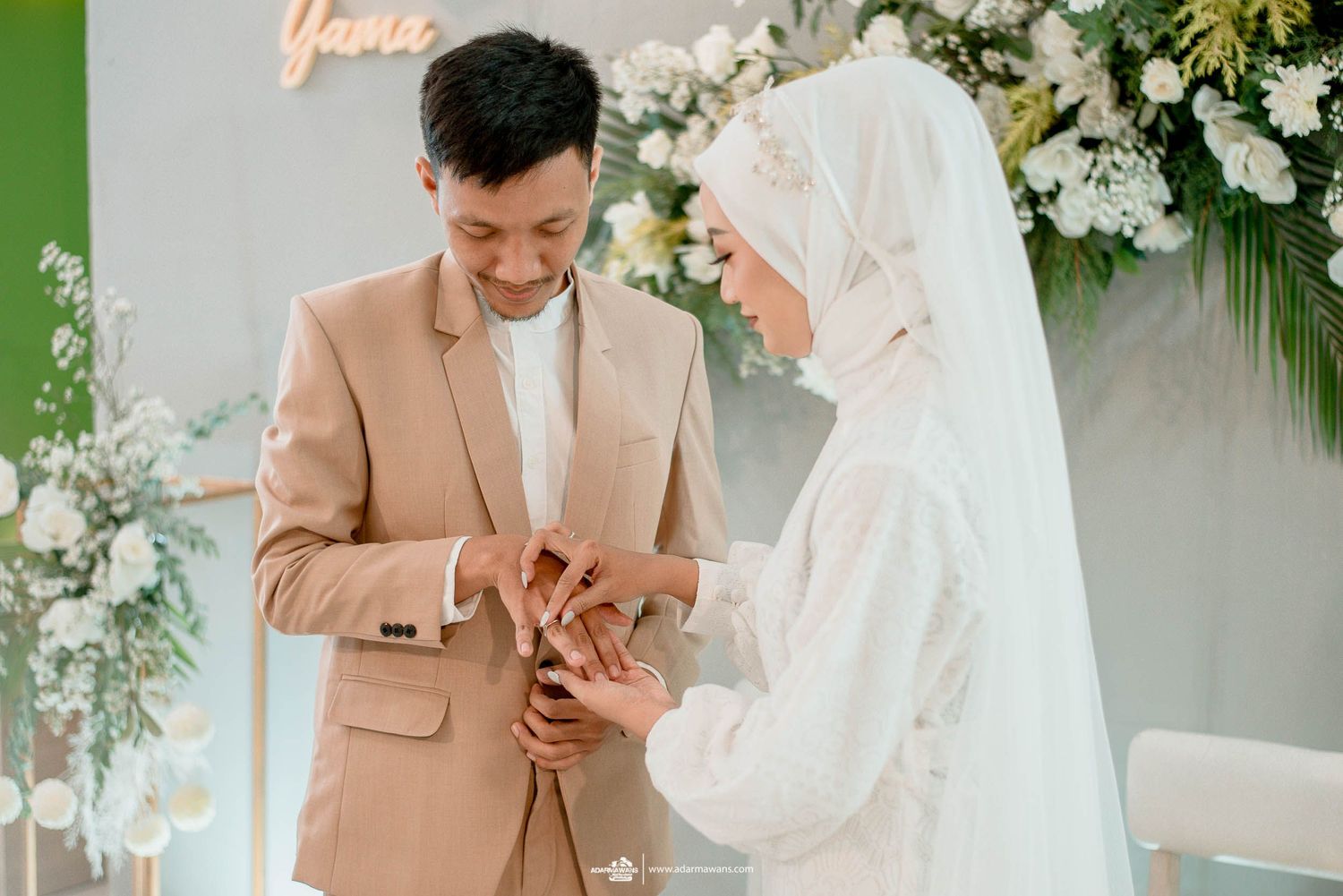 Couple exchanging rings at modern wedding with floral decor and soft lighting.