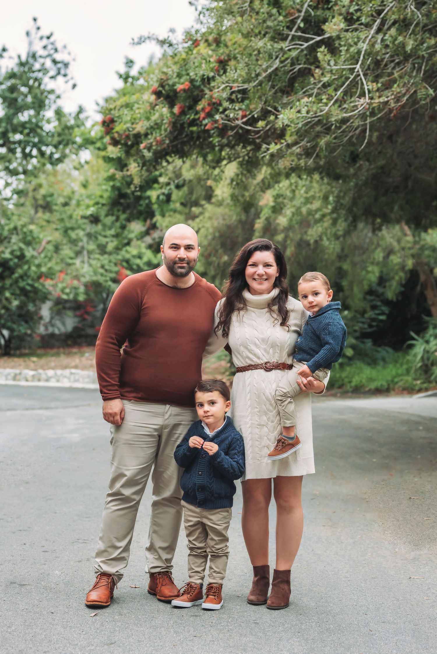 Family of four posing together on a paved path surrounded by lush greenery.