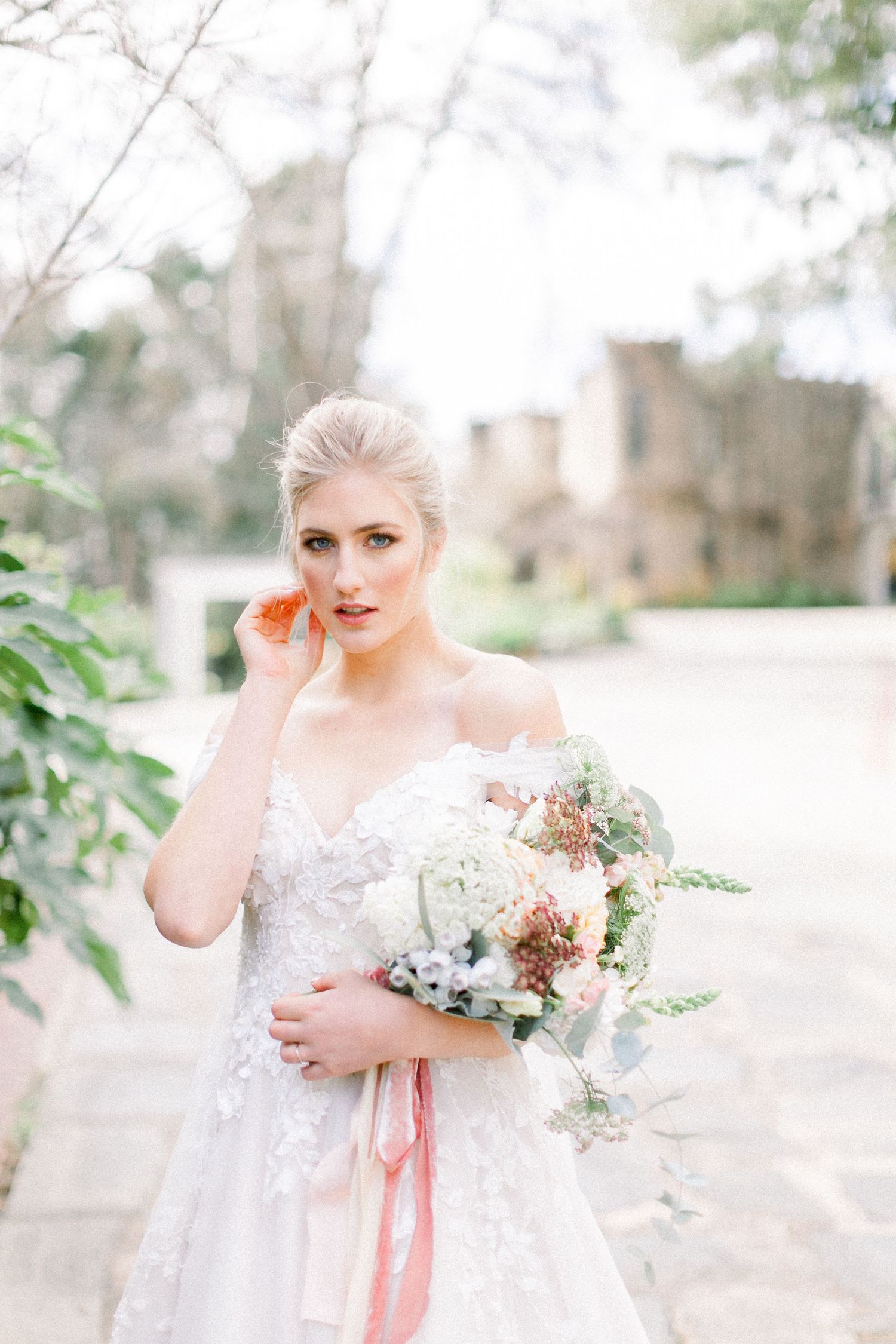 A Bride in a blush lace wedding dress, holding her bouquet with a castle in the background.