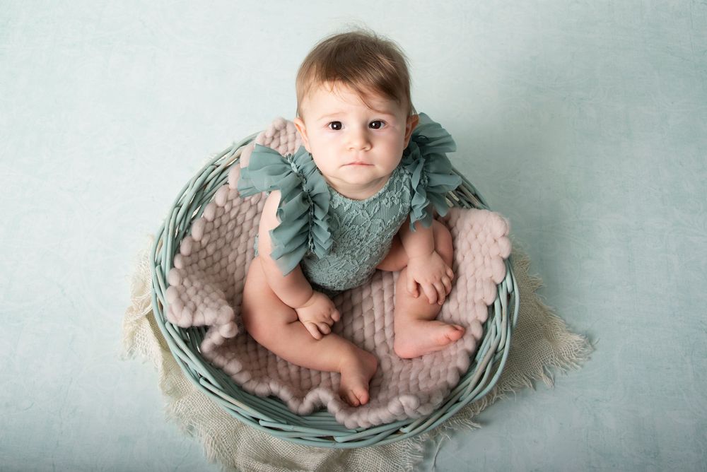 Soft studio portrait on textured blanket in sage tones.