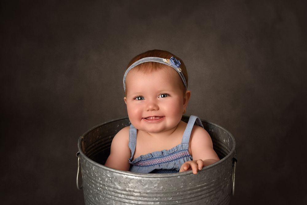 Sweet professional studio portrait with a metal bucket and delicate floral accents against dark background.