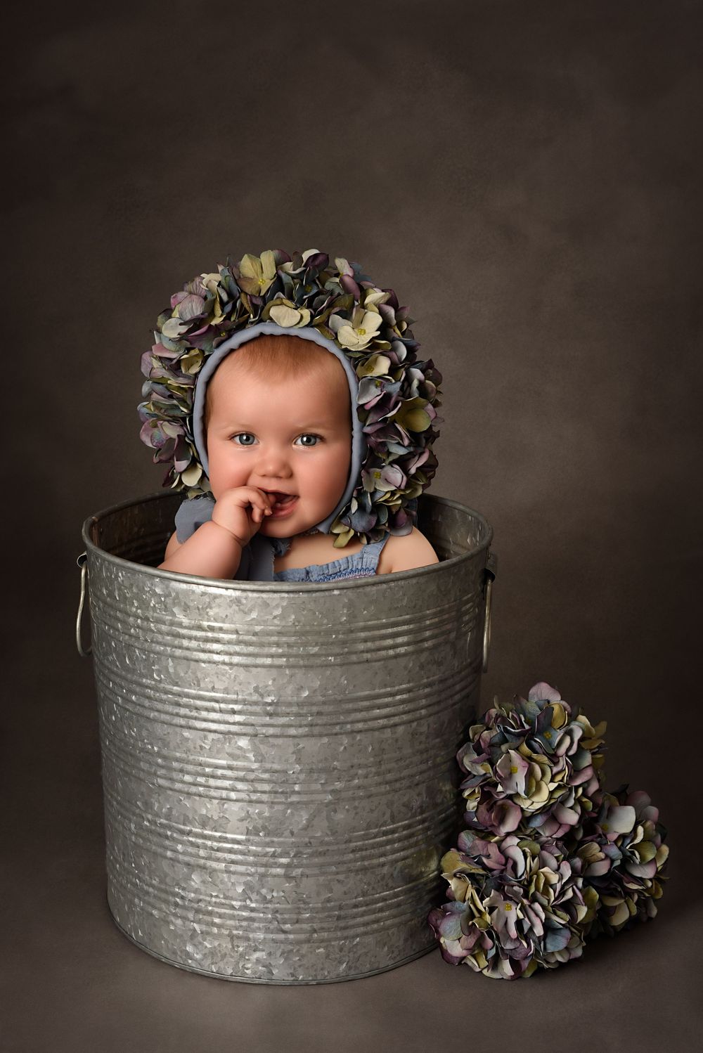 Charming studio with flower bonnet. Portrait featuring a rustic metal container with dried flowers as props.