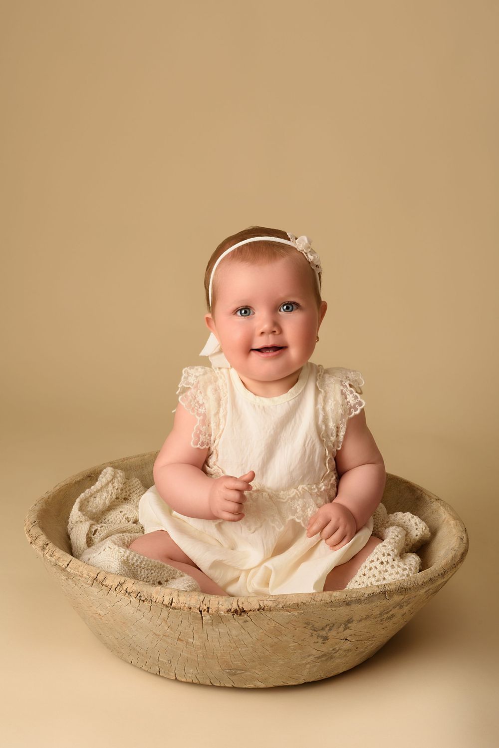Elegant portrait in cream dress sitting in a wooden bowl against neutral background.