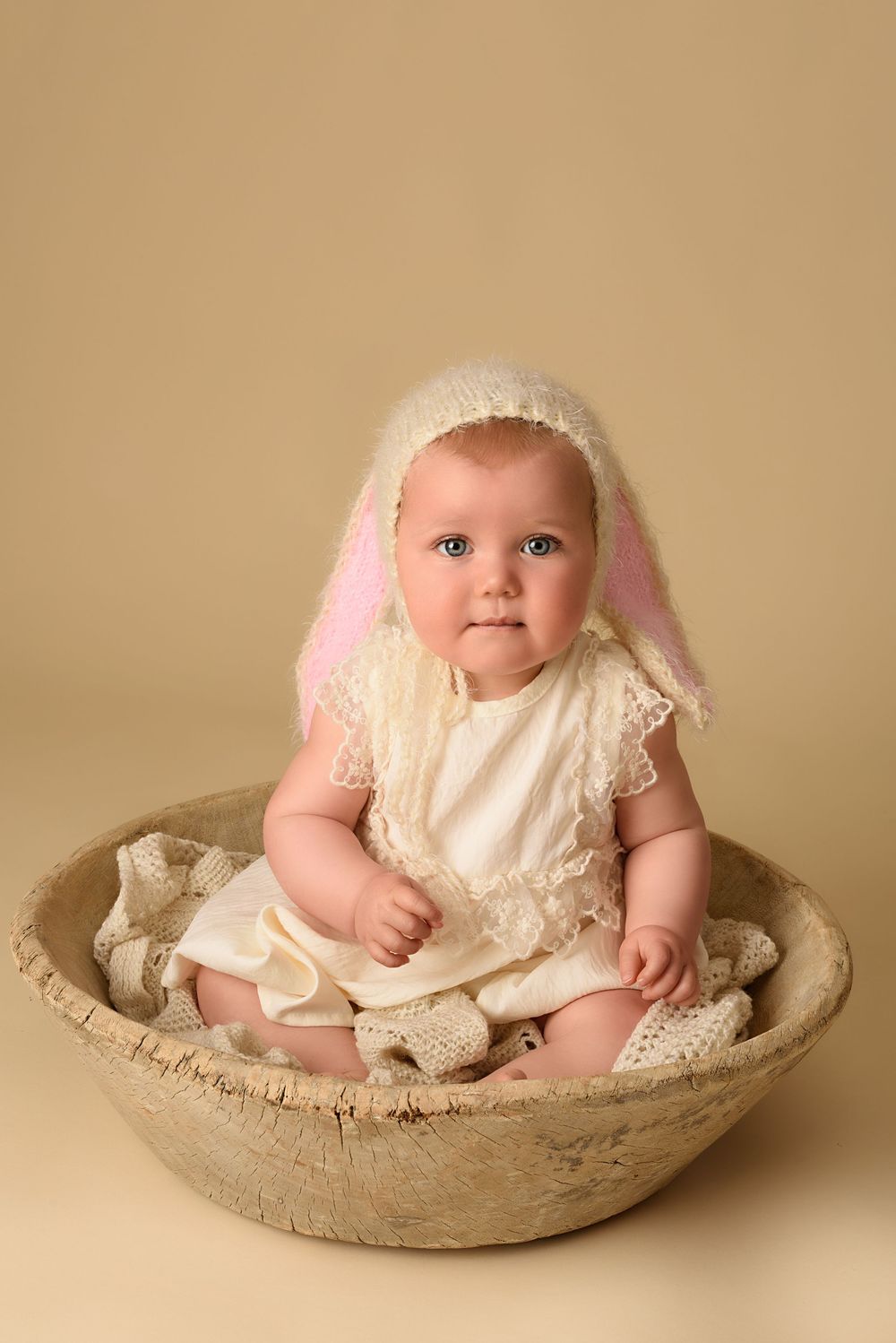 Adorable portrait in white lace dress posed in a decorative wooden bowl.