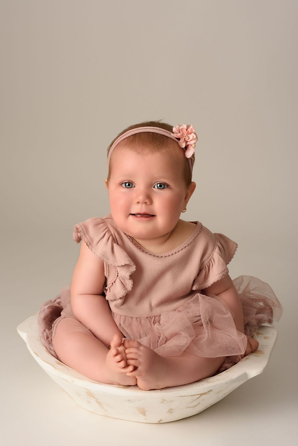 Gentle portrait in dusty rose dress sitting in vintage white bowl against neutral backdrop.