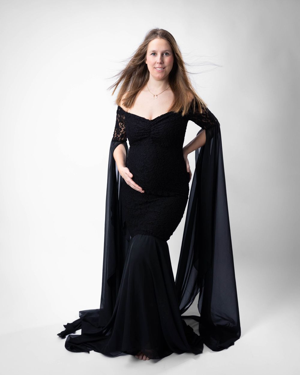 Woman in elegant black evening dress with flowing sleeves poses against white background in studio photoshoot series.