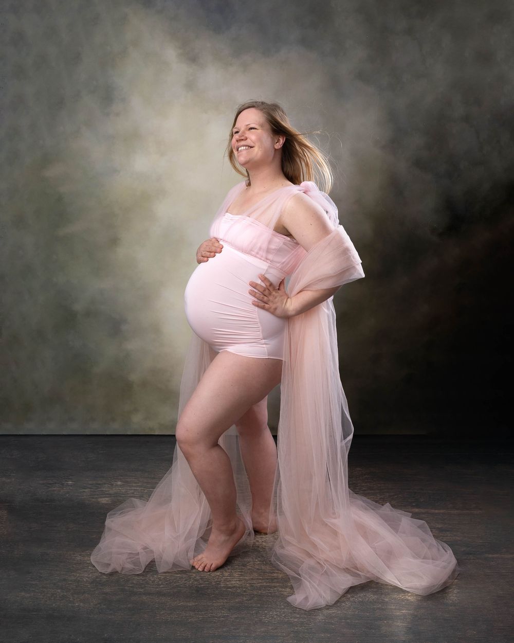 A dreamy maternity photo series in pink tulle against a dark backdrop shows graceful poses and flowing fabric.