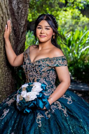 Ornate teal and silver ball gown with off-shoulder design in a garden setting.