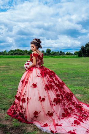 Elegant ball gown with red floral appliques captured in an outdoor setting.