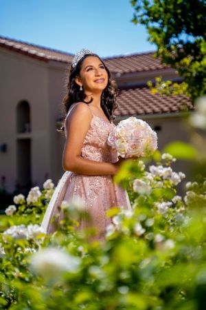 A celebration portrait amid blooming garden roses in a pink beaded gown with crown.