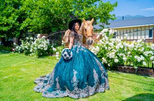 A stunning teal blue quinceañera dress adorned with silver embellishments photographed in a garden setting with a horse.