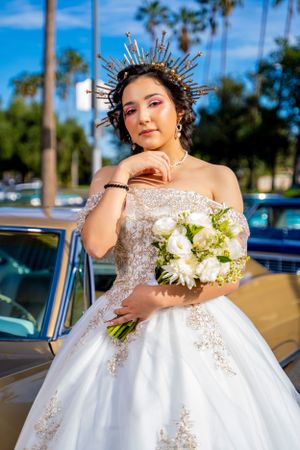 An elegant portrait with sunburst crown and white bouquet beside a classic car. brand park.