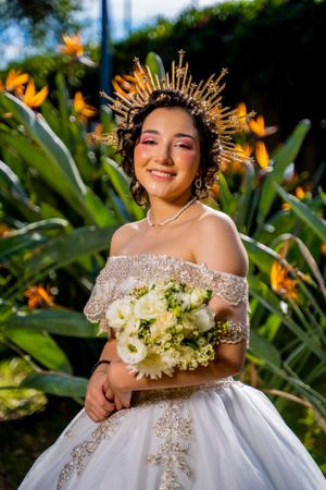 A radiant portrait with golden sunburst crown and white bouquet against tropical flowers.