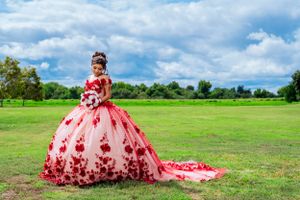 Stunning red and pink ball gown with floral appliques photographed in a green field.
