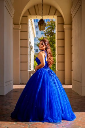 A royal blue ball gown photographed under an elegant archway with Mediterranean architectural details.