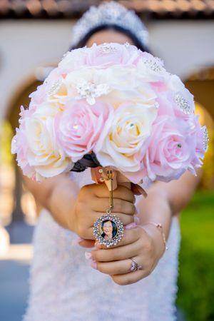 A delicate bouquet of pink and white roses with sparkly details and a locket charm.
