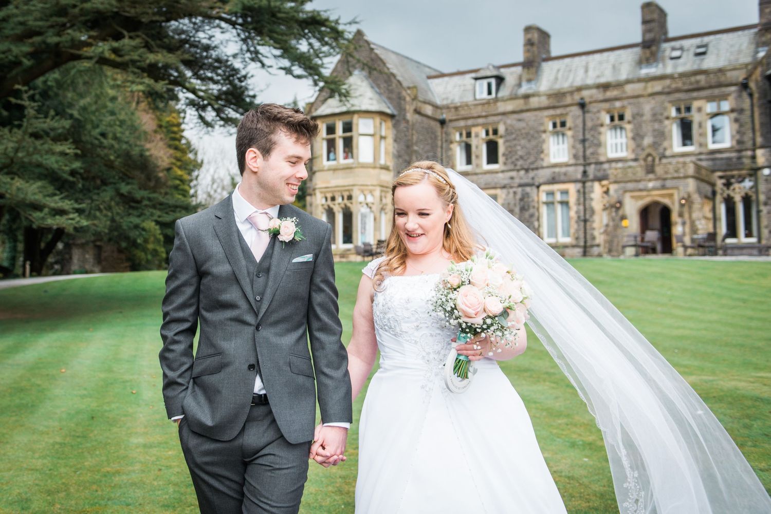 Bride and groom walking in the grounds of The Villa, Levens after their wedding. The brides long veil flies in the wind.