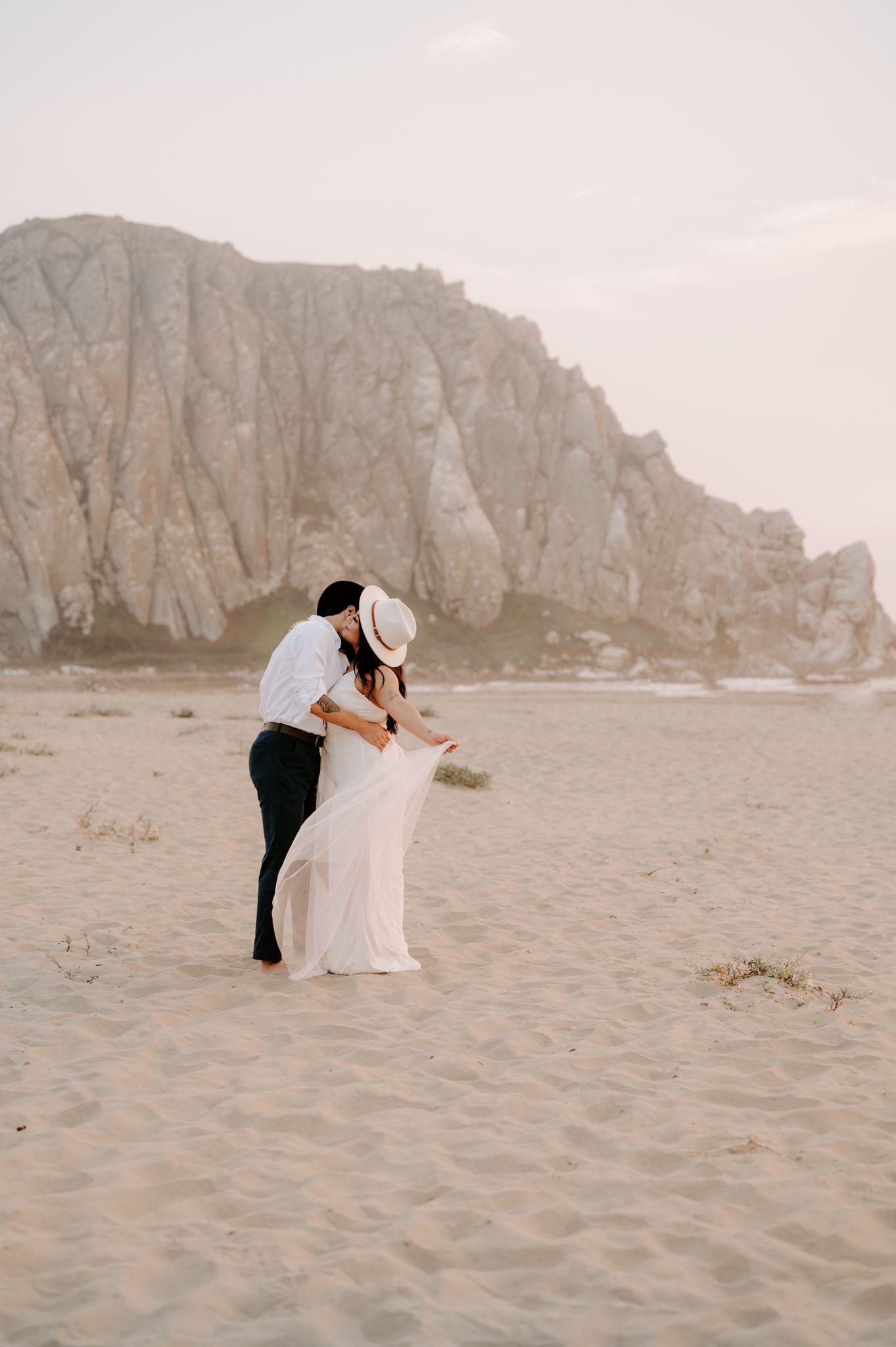 Romantic couple embraces near dramatic coastal cliffs on a sandy beach.