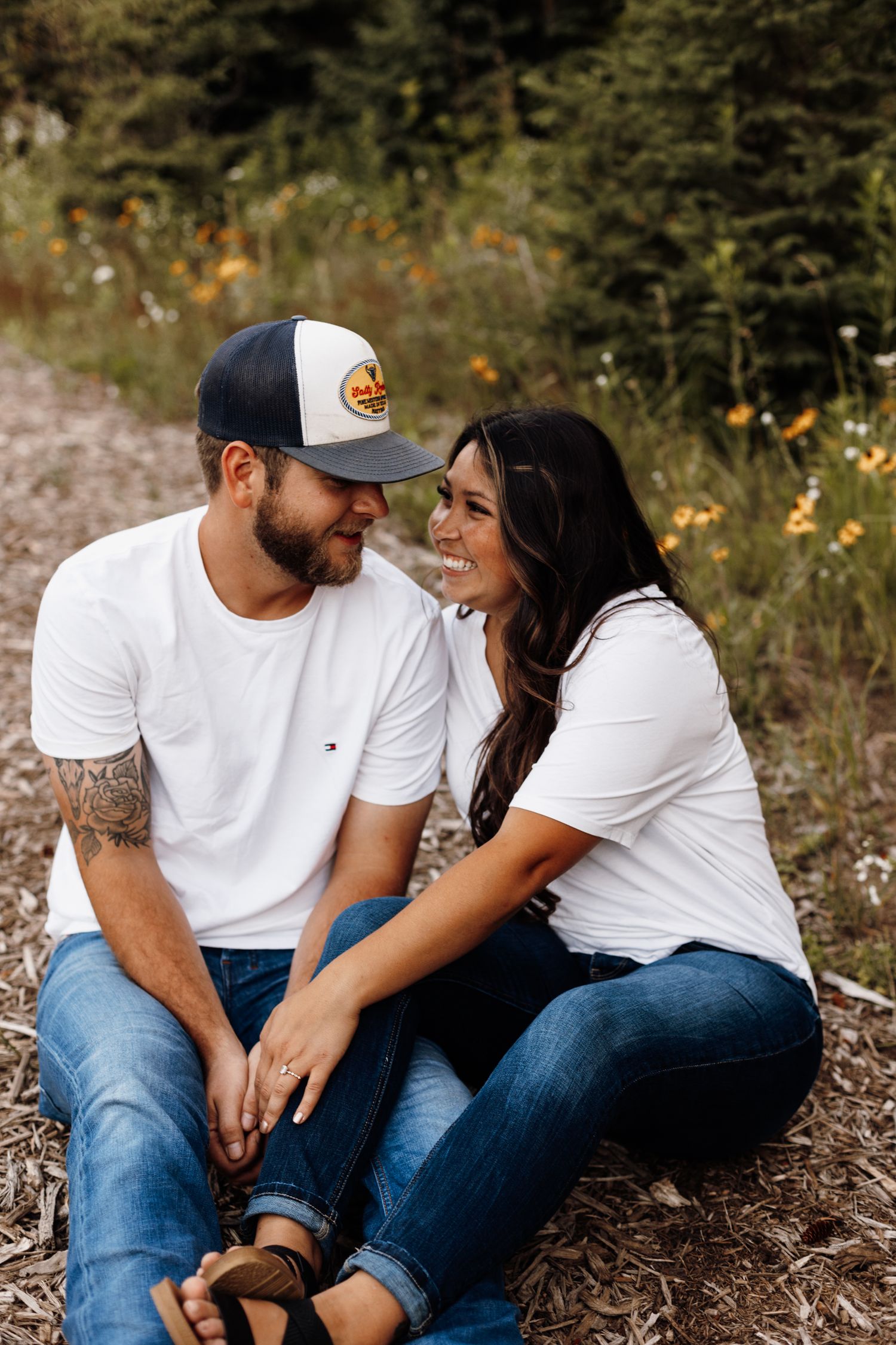 Couple sitting close together and laughing in a wildflower meadow.
